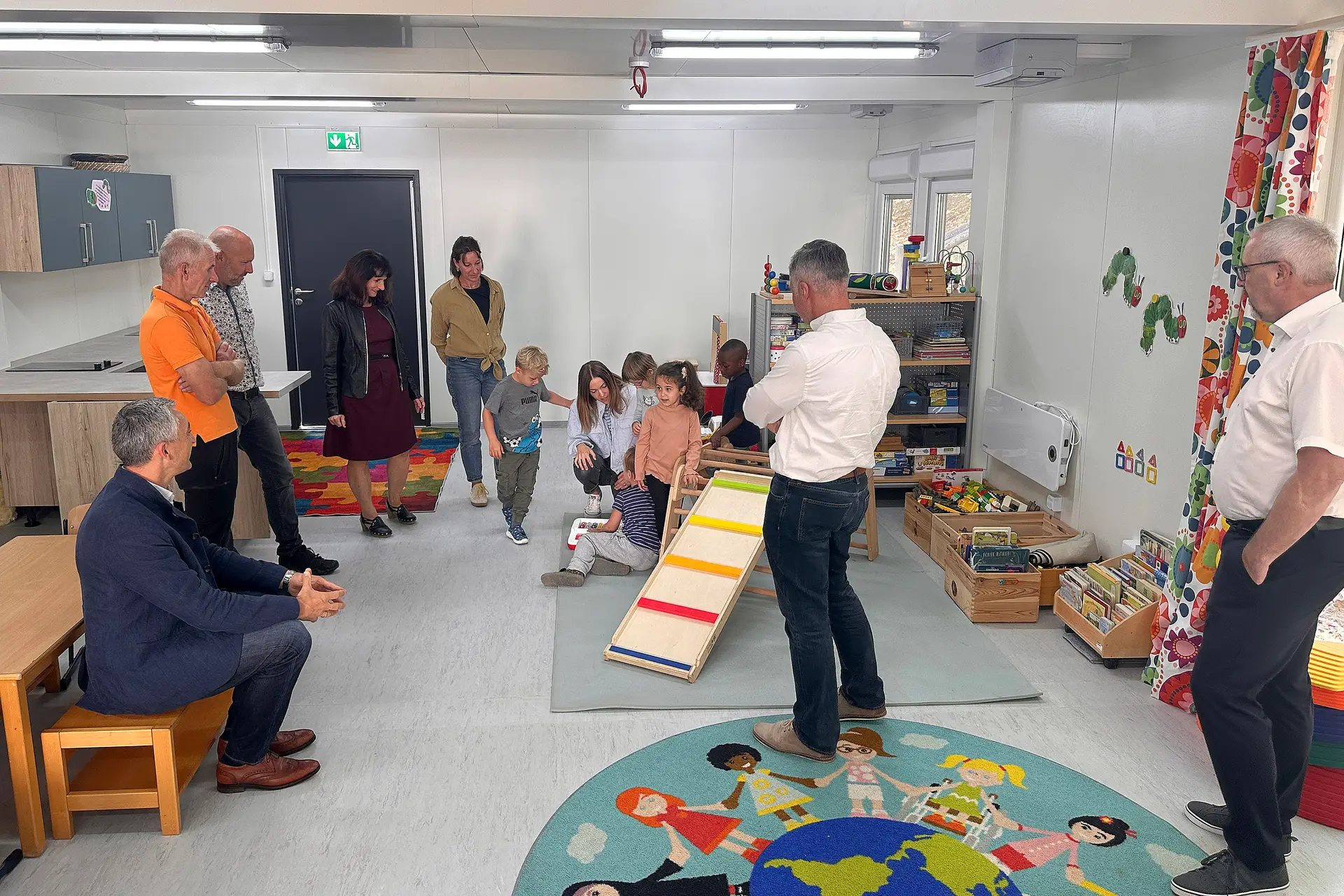 Kinder und Erwachsene erkunden einen Gruppenraum in Containern und beschäftigen sich mit Spielzeug.
